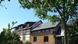 Une maison à deux étages, avec un toit en pente, des fondations en briques et une façade en bois.