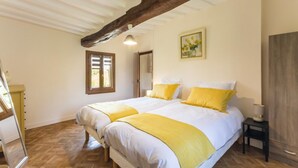 A bedroom with two beds, wooden flooring, a wooden ceiling beam, a window, and a painting on the wall. - Le Bremontier - Massy (MASSY)