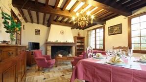 A dining room with a fireplace, wooden beams, a chandelier, and a table set for a meal. - Le Rêve - Preaux - Gîte (PREAUX)
