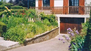 A two-story house with a balcony, surrounded by a garden with various flowers and a stone wall. - Le Rêve - Preaux - Gîte (PREAUX)