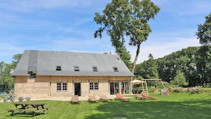 Un bâtiment rustique en pierre, doté d’un toit en pente, d’une terrasse avec des chaises longues en bois et d’une balançoire.