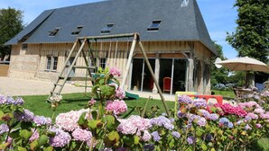 Une grande maison avec un toit en pente, une terrasse en bois et un portique avec des balançoires.