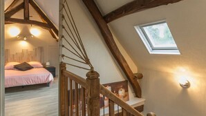 A bedroom with a sloped ceiling, wooden beams, a skylight, and a bed with a pink bedspread. - Le 1722 - Vittefleur (VITTEFLEUR)