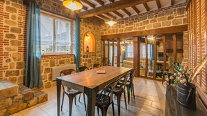 A stone-walled dining area with a wooden table and chairs, a stone bench, and a view through a window. - Le 1722 - Vittefleur (VITTEFLEUR)