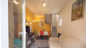 Un espacio habitable compacto con un sofá, una mesa de comedor con sillas, una escalera y un cuadro en la pared.