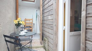 Un pequeño patio con una mesa y sillas, un jarrón de flores amarillas y una puerta de madera.