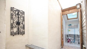 Un estrecho pasillo con una reja metálica decorativa, un pequeño banco y una puerta de madera que da a una habitación con una mesa y sillas.