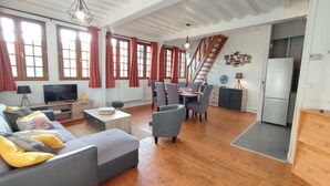 Ein geräumiger Wohnbereich mit einer Sofagarnitur, einem Esstisch mit Stühlen, einer Küchenzeile mit Kühlschrank und einer Treppe, die zu einer oberen Etage führt.