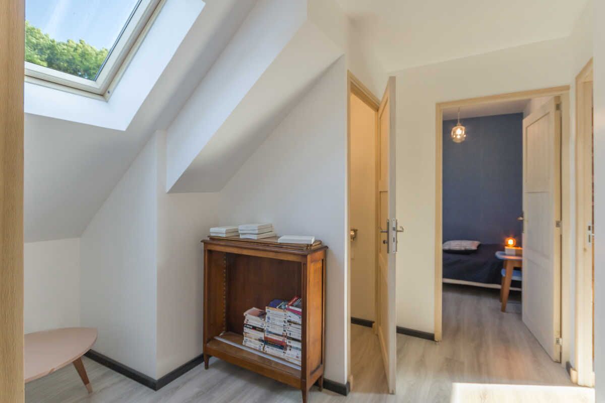 A room with a skylight, a wooden bookshelf, a bed, and a small table with a lamp.