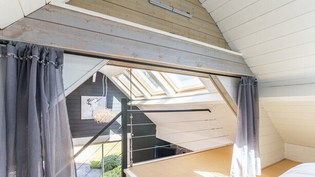 Ein Schlafzimmer mit schrägen Wänden, einem Oberlicht und Blick auf eine Treppe, die zu einer oberen Ebene führt.