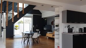 Eine moderne Küche mit schwarzen Schränken, eine Essecke mit Tisch und Stühlen und eine Treppe, die zu einem Balkon führt.