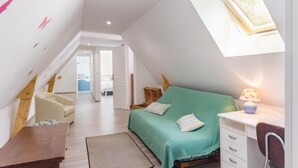 A bedroom with a sloped ceiling, a bed with a green bedspread, a desk with a lamp, and a chair.