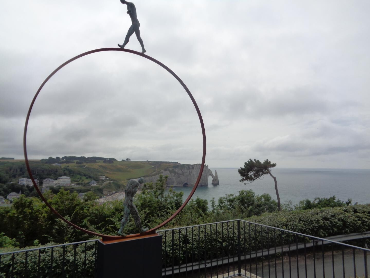 A sculpture of a person balancing on a large circular ring, with a coastal landscape in the background.
