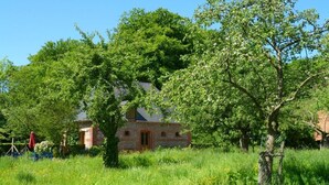 A rustic stone house surrounded by lush greenery and a field of yellow flowers.