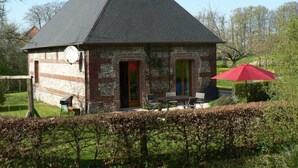 A small brick house with a sloped roof, a chimney, and a small patio with a table and chairs.