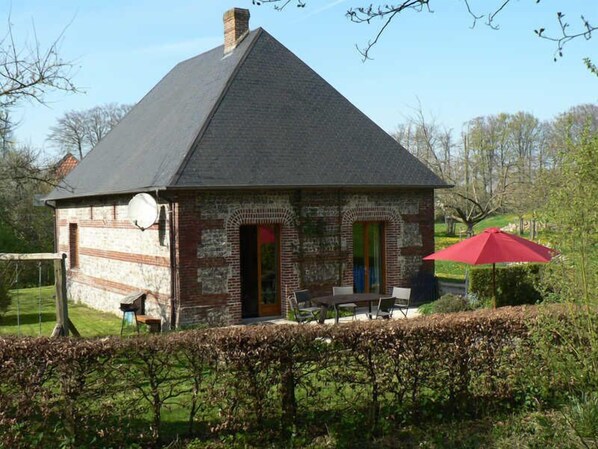 A small brick house with a sloped roof, a chimney, and a small patio with a table and chairs.