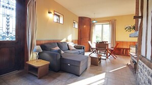 A living room with a sectional sofa, a small table, and a lamp. There is a dining area with a table and chairs.