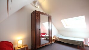 Un dormitorio con un armario grande de madera, una cama individual, una mesita de noche pequeña con una lámpara y un tragaluz.