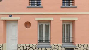 Ein Gebäude mit rosa Fassade, Nummer 74, mit drei Fenstern und schwarzen Geländern, einer weißen Tür und einem kleinen Rundfenster.