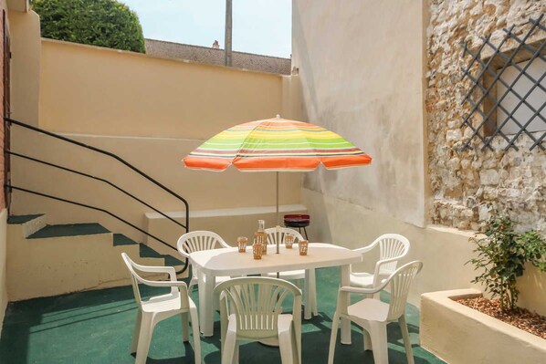 A patio with a table and chairs, a striped umbrella, and a stone wall.