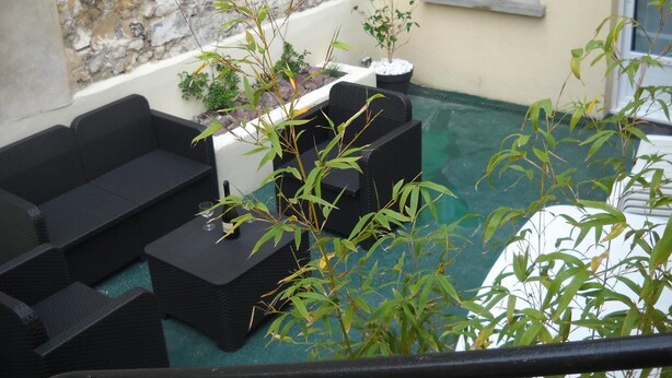 Eine Terrasse mit schwarzer Gartenmöbeln, einer Steinmauer und Topfpflanzen.