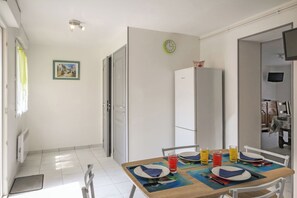 Un coin repas avec une table dressée pour quatre personnes, un réfrigérateur et une horloge au mur.