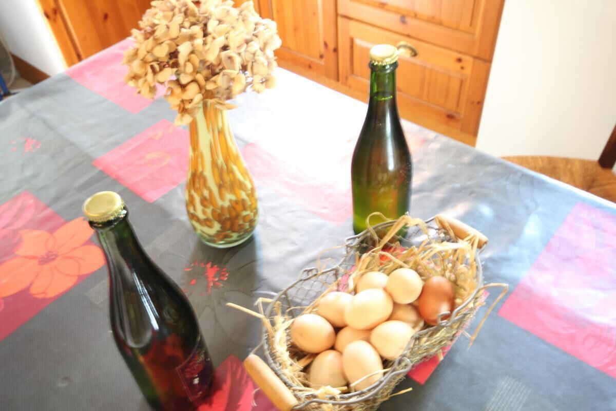 Une table recouverte d’une nappe à motifs floraux, avec deux bouteilles et un panier d’œufs.