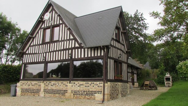 Ein traditionelles Fachwerkhäuschen mit Steinunterbau, großen Fenstern und einem Schotterweg.