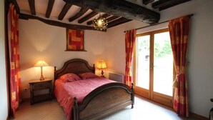 Ein Schlafzimmer mit einem hölzernen Bett, zwei Nachttischlampen, einem Fenster mit Vorhängen und einer Decke mit sichtbaren Balken.