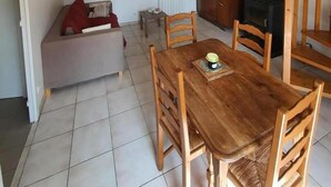 A dining area with a wooden table and chairs, a sofa, a television, and a wood-burning stove. - Rose - Bourg DUN (BOURG DUN (LE))