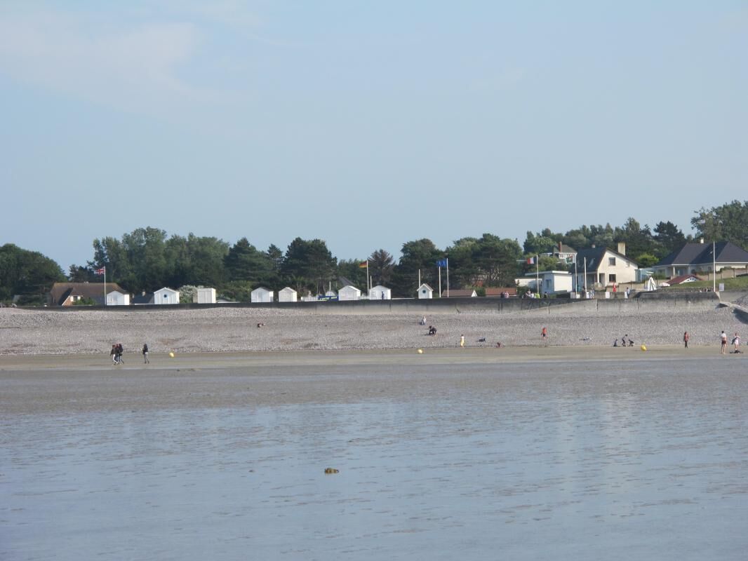 Una playa con gente, una hilera de edificios blancos pequeños y algunas casas más grandes al fondo.