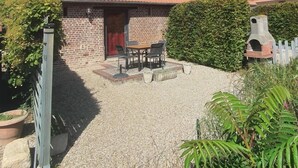 A brick building with a red-tiled roof, a small patio with a table and chairs, and a brick chimney. - Rose - Bourg DUN (BOURG DUN (LE))