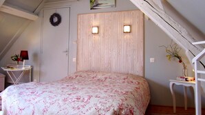 A bedroom with a wooden headboard, a floral bedspread, a small table with a vase, and a painting on the wall. - La Cécilève - Riville (RIVILLE)