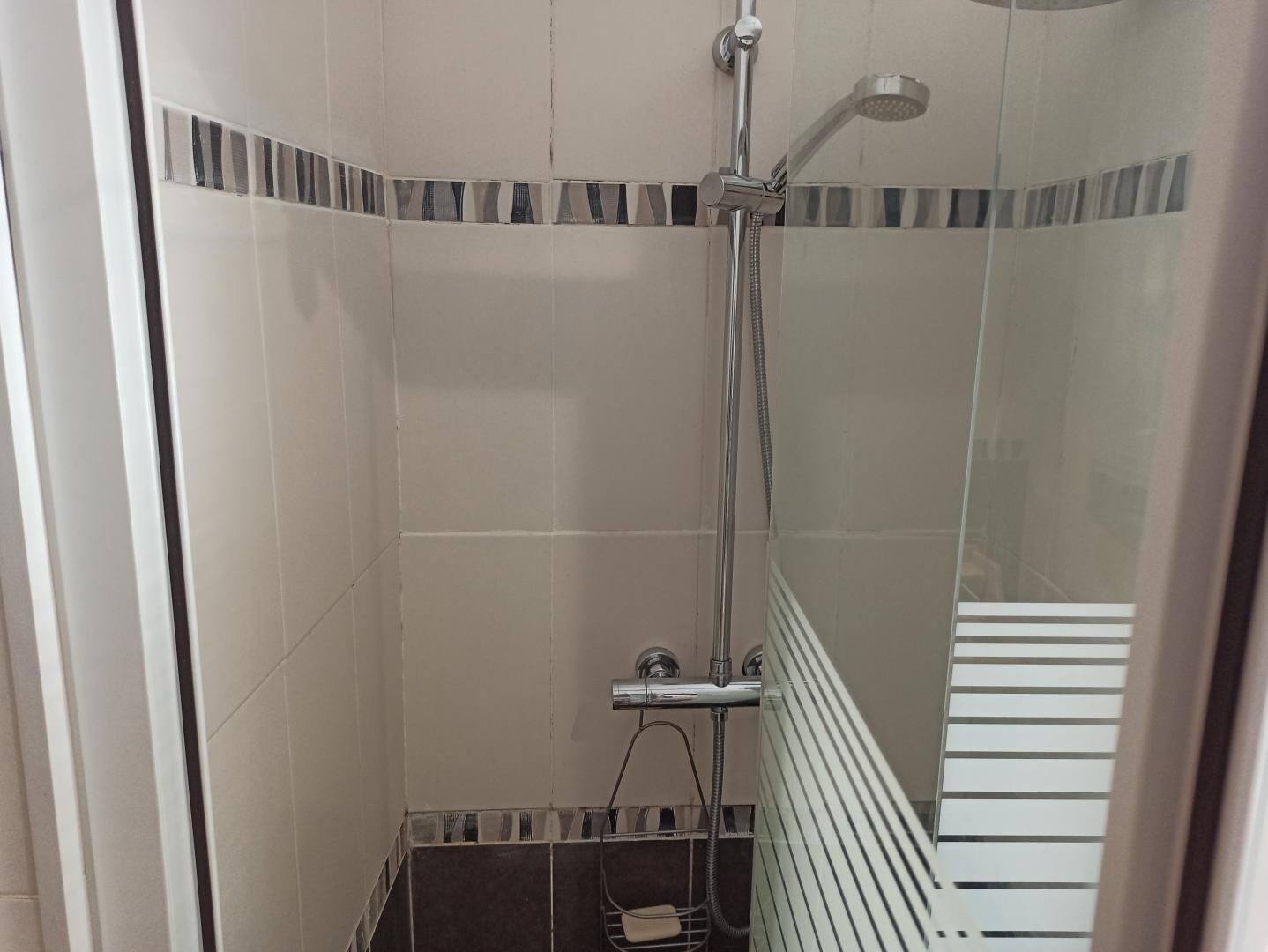 A shower area with a glass door, a towel rack, and a tiled floor.