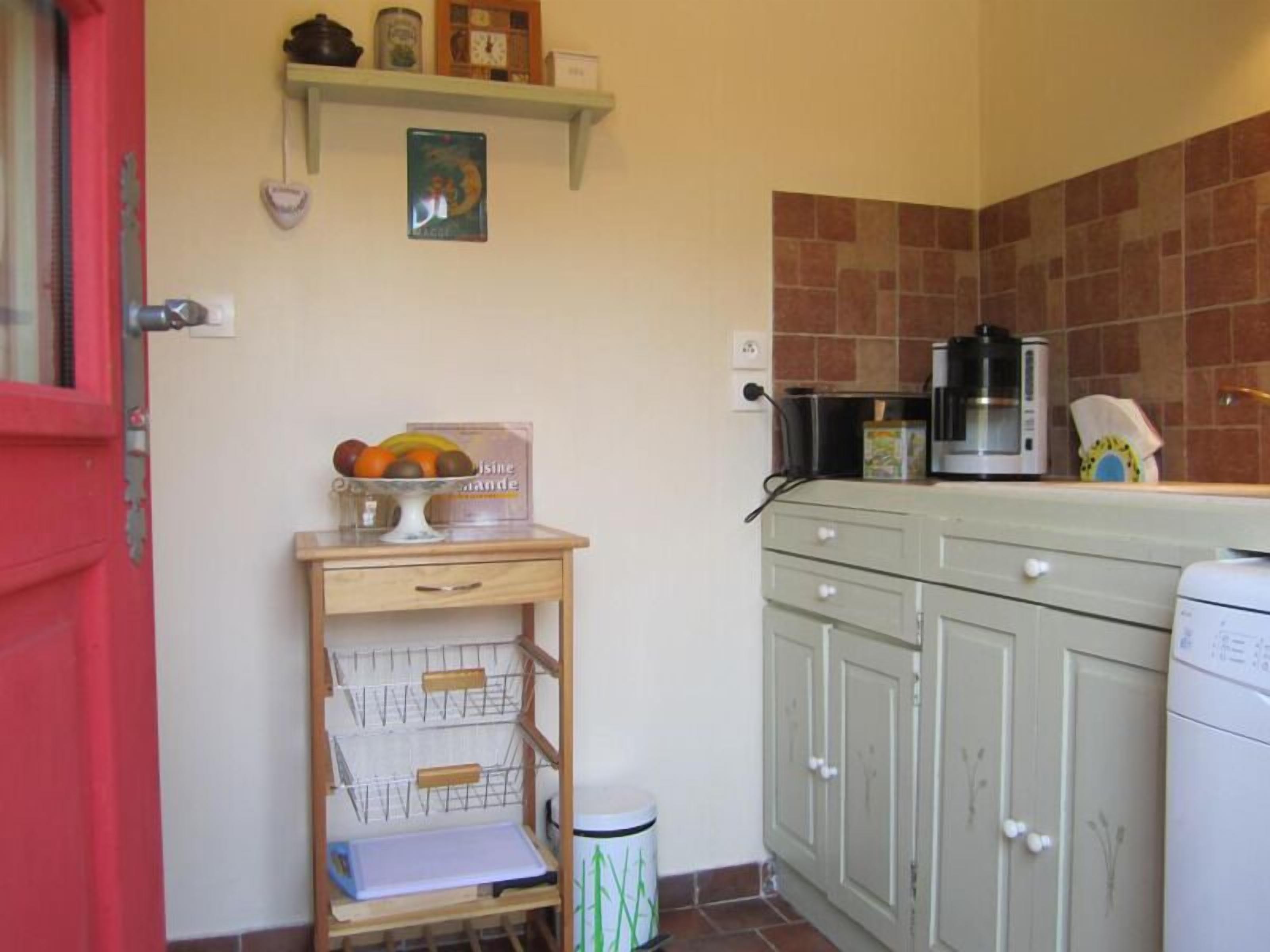 Una cocina con una puerta roja, un frutero en un estante, una cafetera y un microondas.