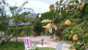 An outdoor seating area with two white chairs and a table, surrounded by lush greenery and fruit trees. - La Cécilève - Riville (RIVILLE)