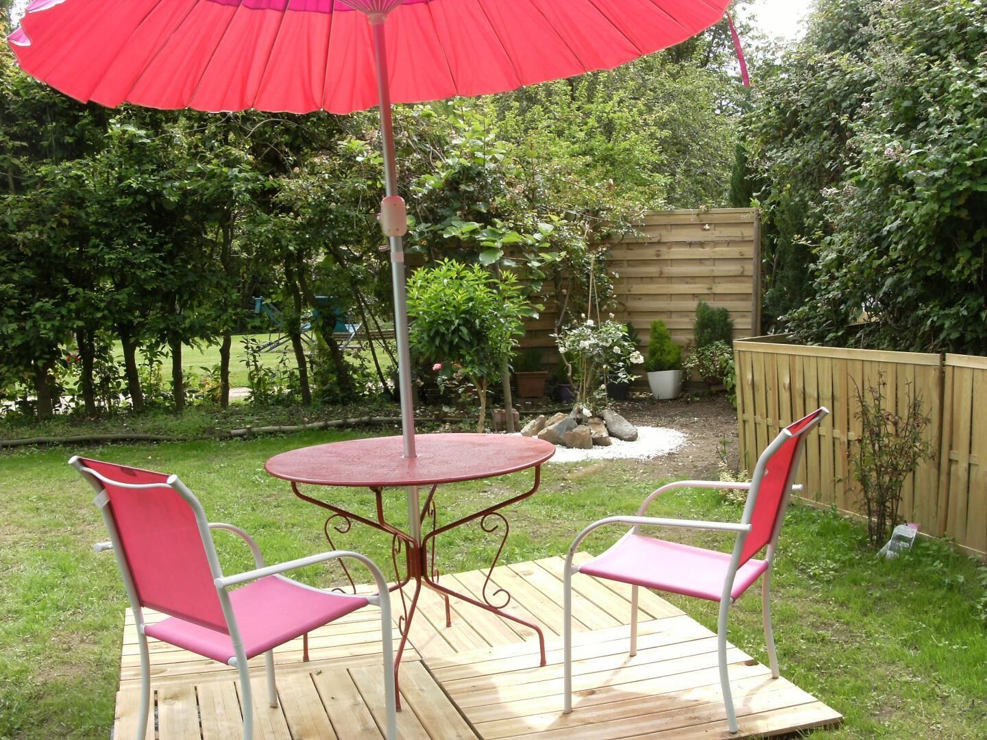 Een terras met een ronde tafel, twee stoelen, een parasol en een houten terras.
