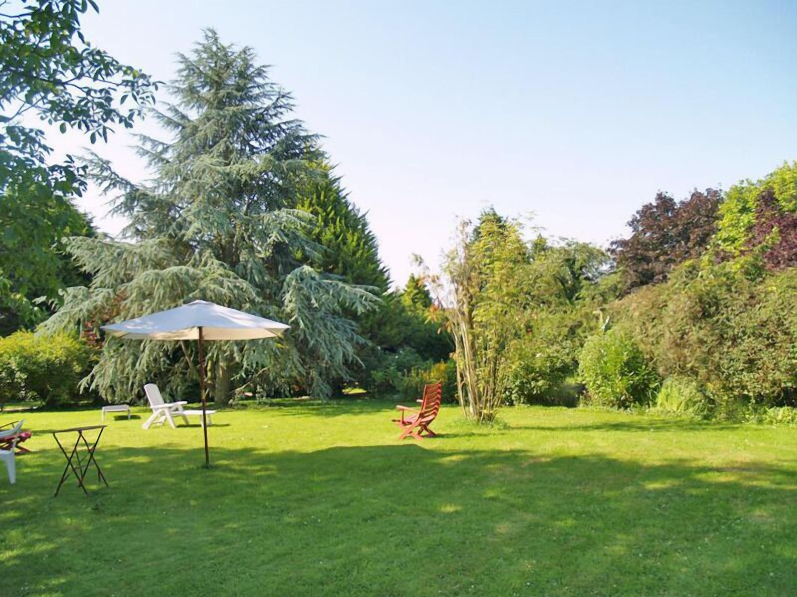 A well-maintained garden with a lawn, a patio area with a table and chairs, and a variety of trees and shrubs.