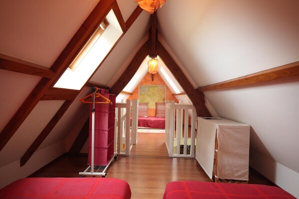 Un dormitorio abuhardillado con vigas de madera, un tragaluz, una cama, una cuna y un sillón colgante.
