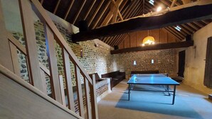 A spacious room with a ping pong table, a wooden staircase, and exposed wooden beams on the ceiling.