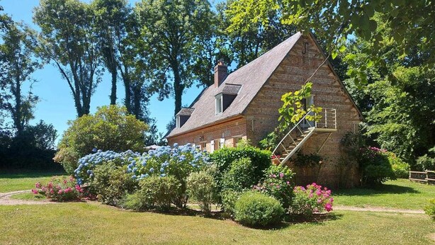 A stone house with a steeply pitched roof, a visible chimney, and a wooden staircase leading to the entrance.