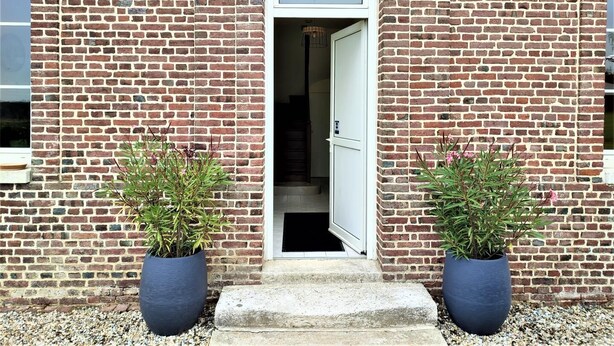 Un bâtiment en briques avec une porte blanche et deux plantes en pot de chaque côté.