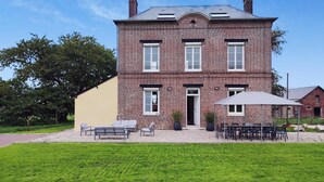 Une maison à deux étages, construite en briques, avec un porche à l’avant, un patio couvert aménagé avec du mobilier d’extérieur et une pelouse bien entretenue.