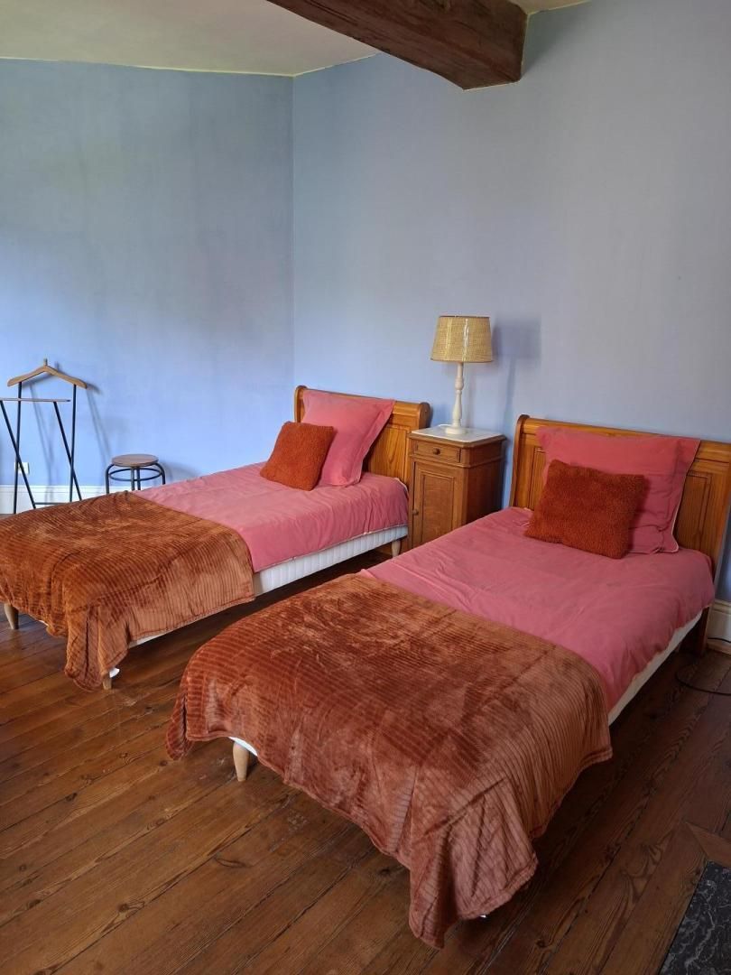 A bedroom with two beds, wooden flooring, a nightstand with a lamp, and a small stool.