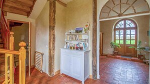 Una habitación rústica con vigas de madera a la vista, un armario blanco lleno de libros y un amplio ventanal de arco.