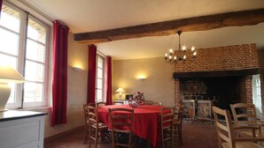 Un comedor con chimenea de ladrillo, vigas de madera y mantel rojo.