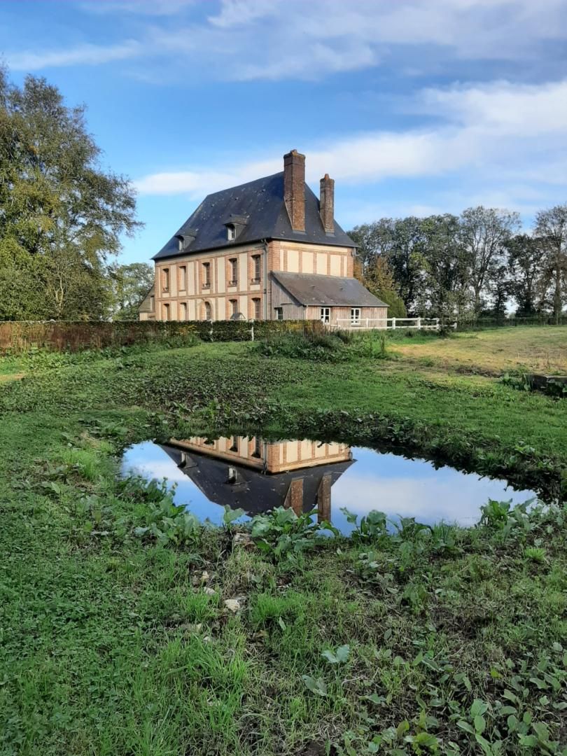 Un grand bâtiment historique à la façade symétrique, doté d’une cheminée centrale et dont l’image se reflète dans un étang.