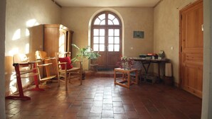 Una habitación con una silla de madera, una mesa con libros, una planta en maceta y un ventanal arqueado grande.