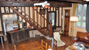 A rustic interior with a wooden staircase, a kitchen area, a dining table with chairs, and a leather sofa. - Le Verger - Varneville Bretteville (VARNEVILLE BRETTEVILLE)