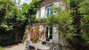 A rustic stone building with a garden patio featuring a table and chairs. - Le Verger - Varneville Bretteville (VARNEVILLE BRETTEVILLE)